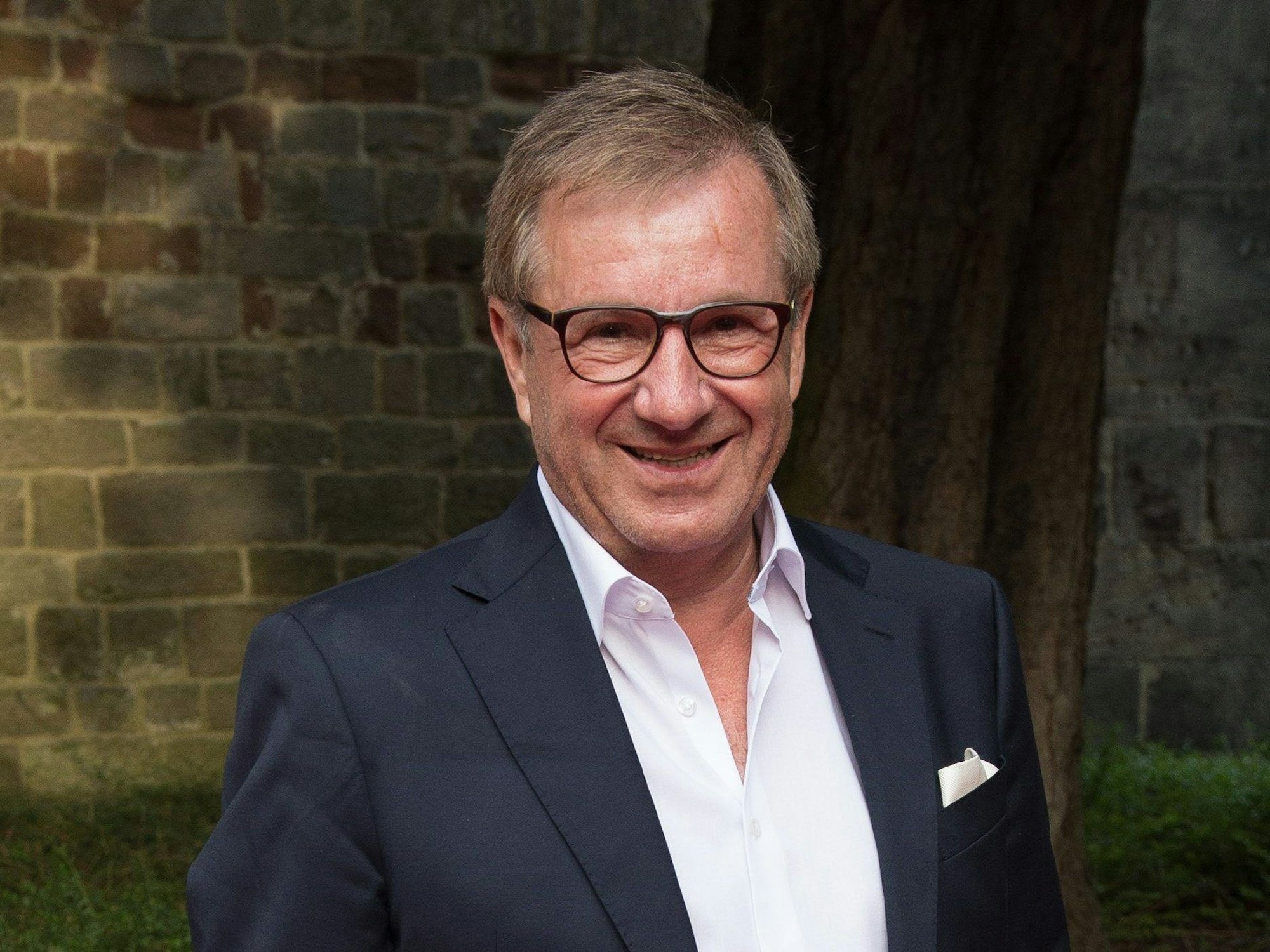 Jan Hofer, Moderator und ehemaliger Tagesschau-Sprecher, steht vor einer Backsteinwand und lächelt in die Kamera.