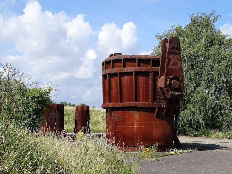 Rostige Industriebehälter mit Gras, Bäumen und Wolkenhimmel