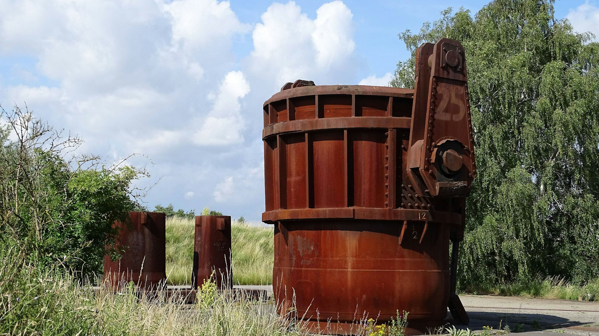 Rostige Industriebehälter mit Gras, Bäumen und Wolkenhimmel