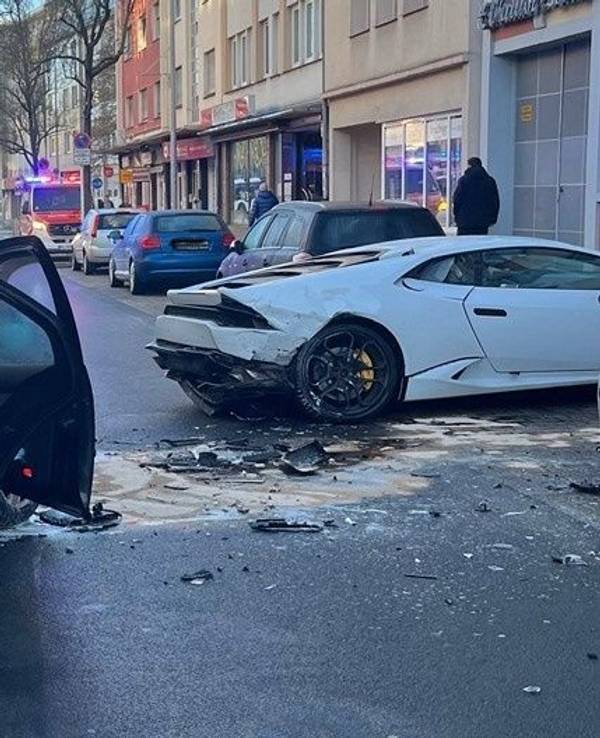 Zwei beschädigte Unfallwagen, darunter ein Lamborghini stehen auf einer Fahrbahn, im Hintergrund Einsatzkräfte und - fahrzeuge von Feuerwehr und Rettungsdienst.