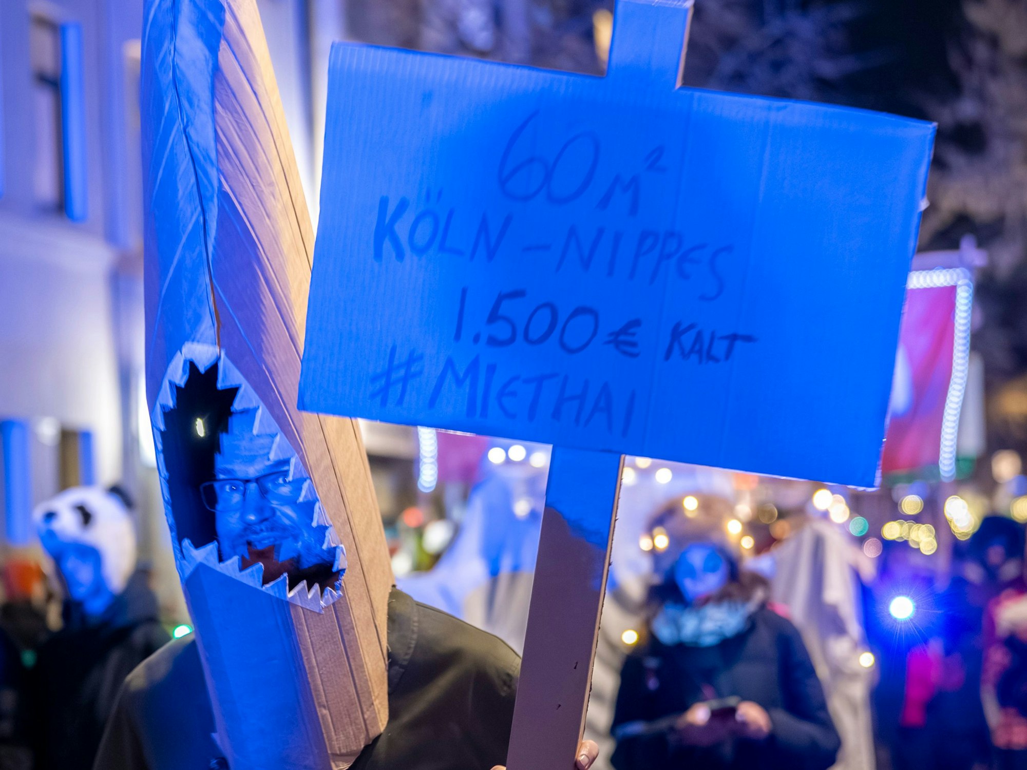 Eine Person ist als Hai verkleidet und trägt ein Schild auf dem er eine Miete von 1500 Euro kalt für eine 60- Quadratmeter-Wohnung in Nippes anprangert.