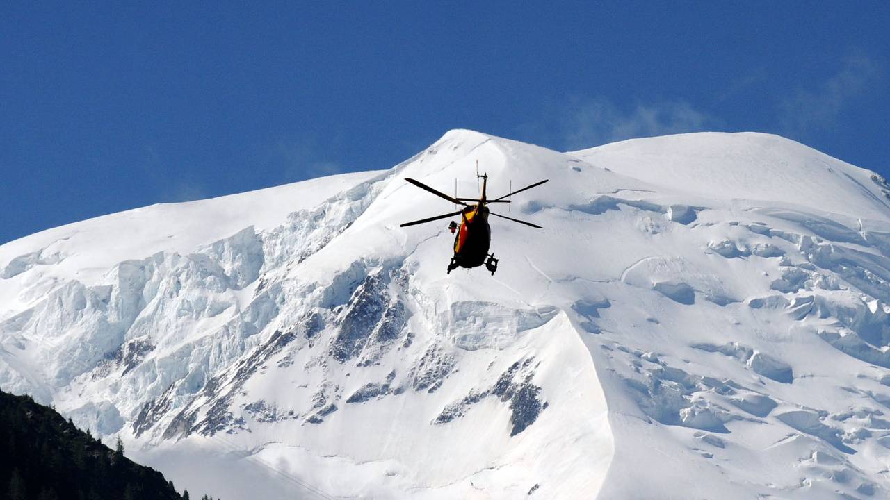Ein Hubschrauber fliegt über schneebedeckte Berge.
