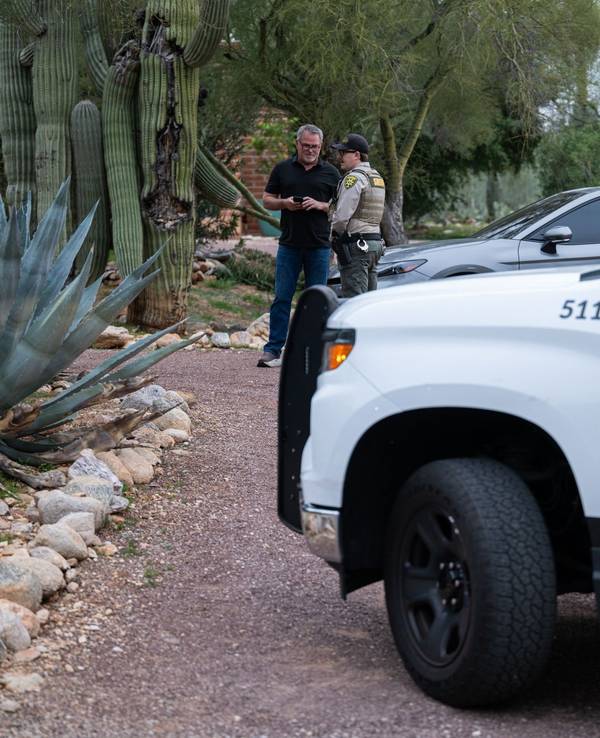 Ein Beamter des Pima County Sheriffs unterhält sich mit einem privaten Sicherheitsbeamten vor dem Haus von Nancy Guthrie. Auf der Türschwelle wurden Blutspuren der Entführten gefunden.