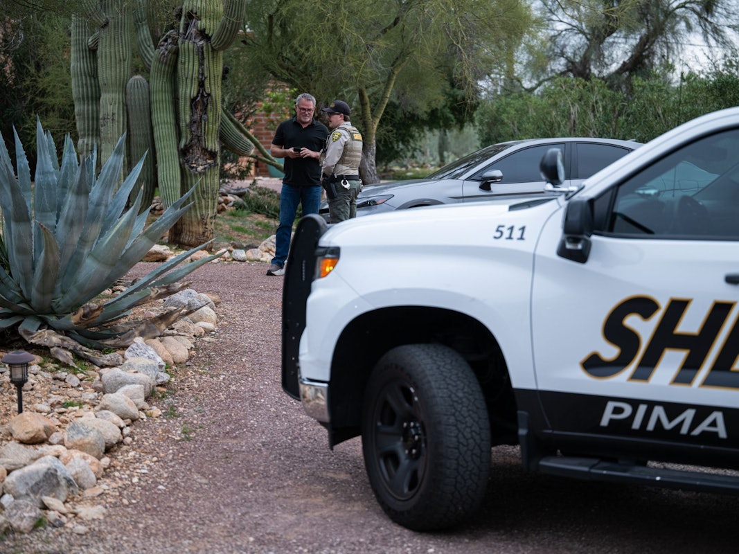 Ein Beamter des Pima County Sheriffs unterhält sich mit einem privaten Sicherheitsbeamten vor dem Haus von Nancy Guthrie. Auf der Türschwelle wurden Blutspuren der Entführten gefunden.