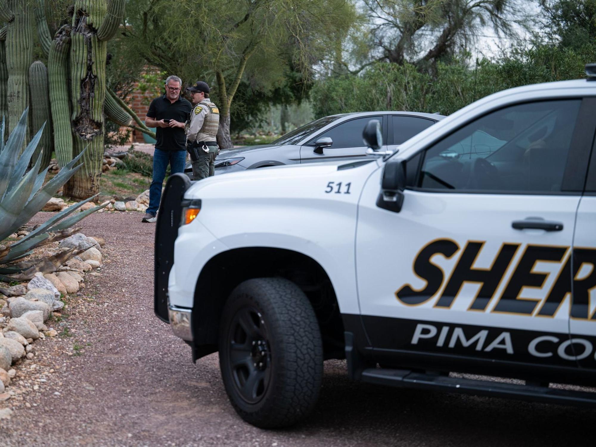 Ein Beamter des Pima County Sheriffs unterhält sich mit einem privaten Sicherheitsbeamten vor dem Haus von Nancy Guthrie. Auf der Türschwelle wurden Blutspuren der Entführten gefunden.