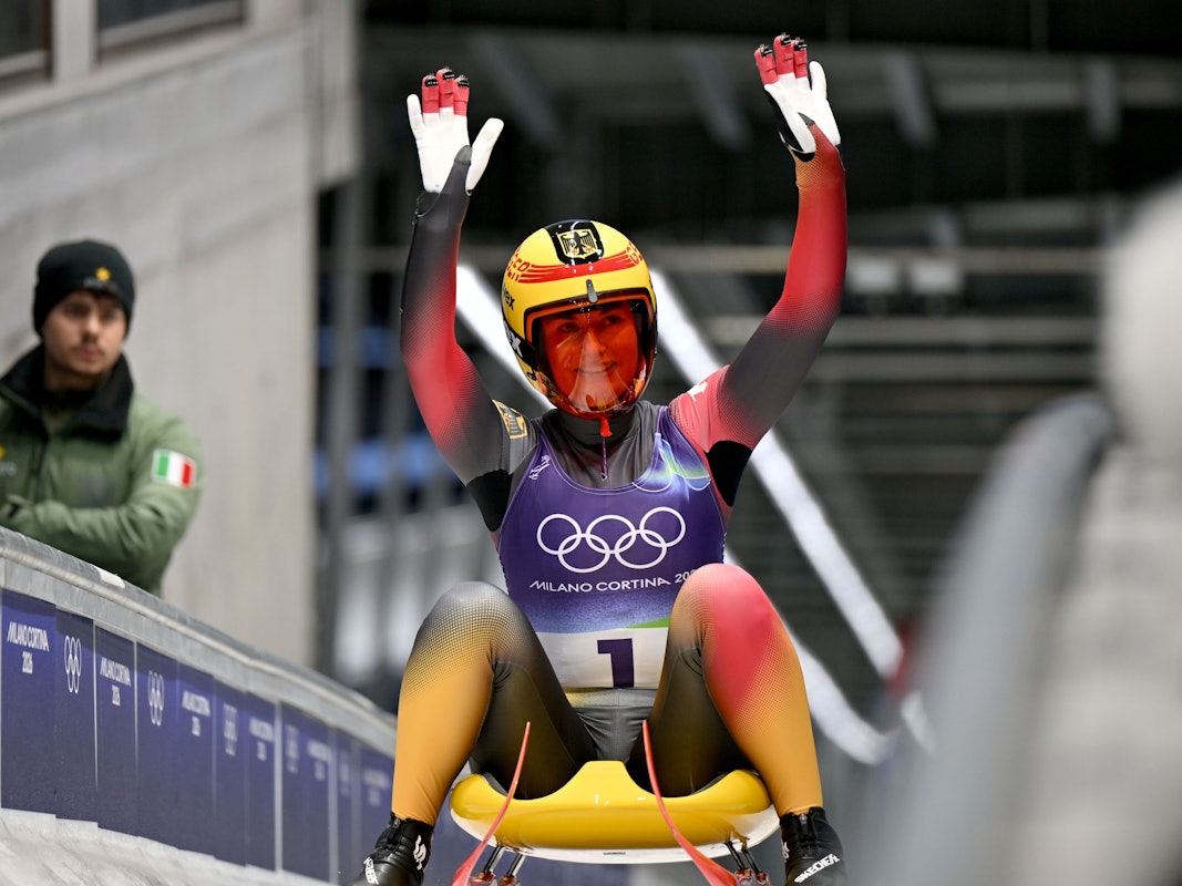 Julia Taubitz sitzt auf ihrem Schlitten und winkt.