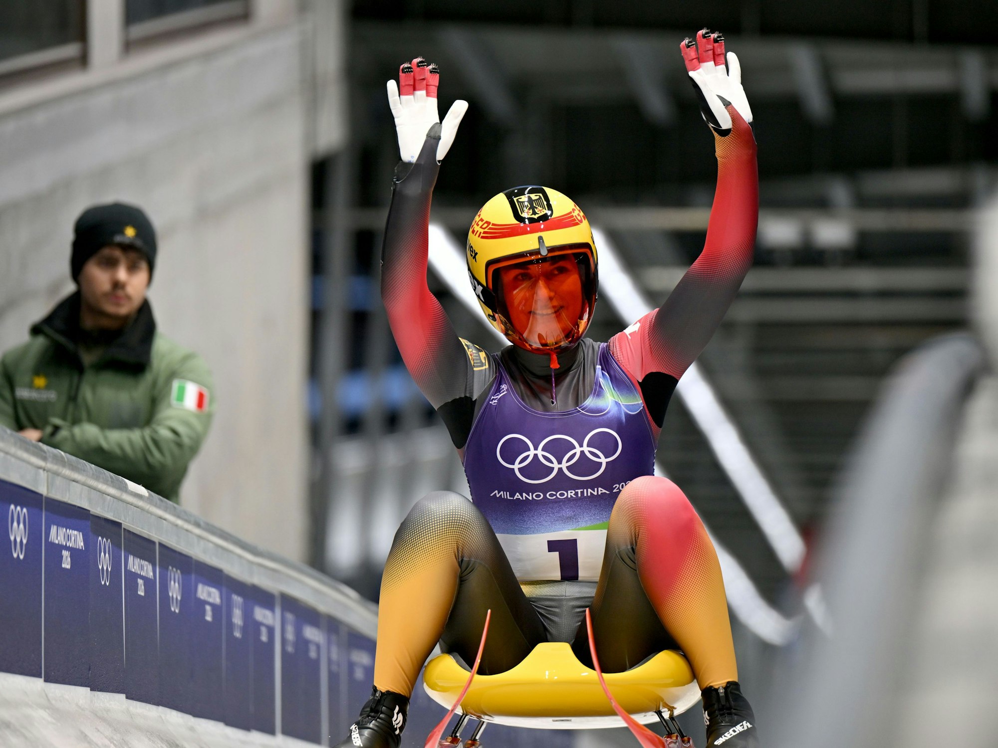 Julia Taubitz sitzt auf ihrem Schlitten und winkt.