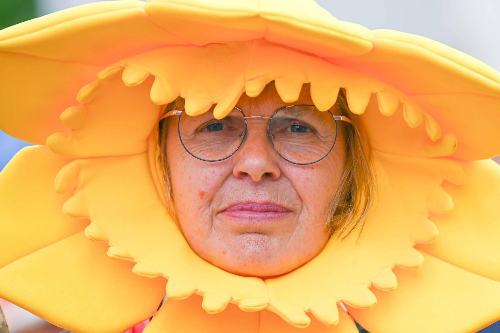 Überdimensionale Hüte schützen. Mit Klarsichtfolie umwickelt, halten sie auch Regen ab. Eine Frau trägt einen großen gelben Hut.