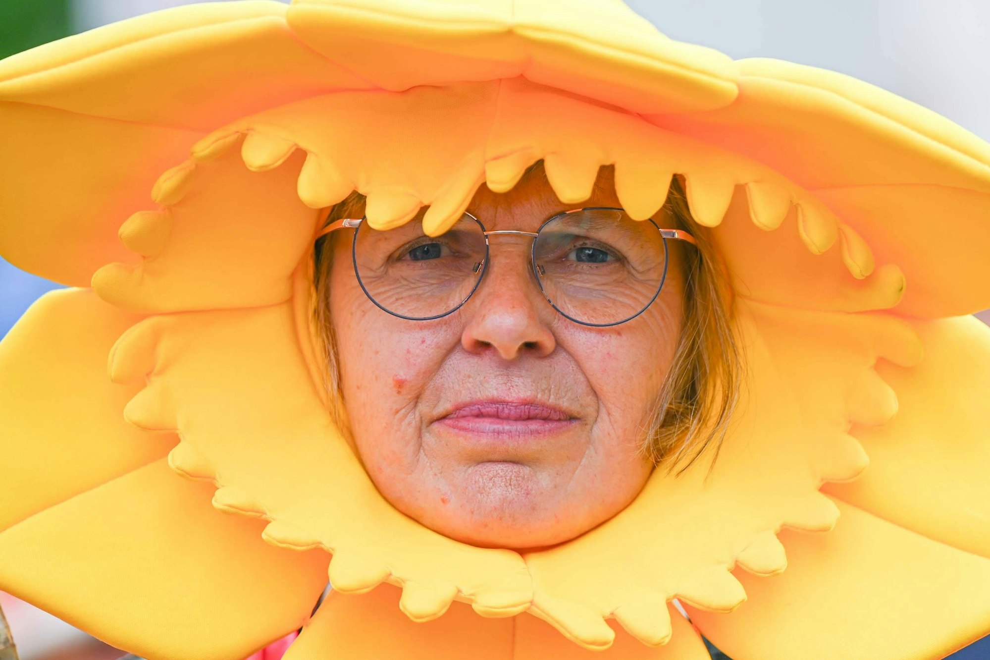 Überdimensionale Hüte schützen. Mit Klarsichtfolie umwickelt, halten sie auch Regen ab. Eine Frau trägt einen großen gelben Hut.