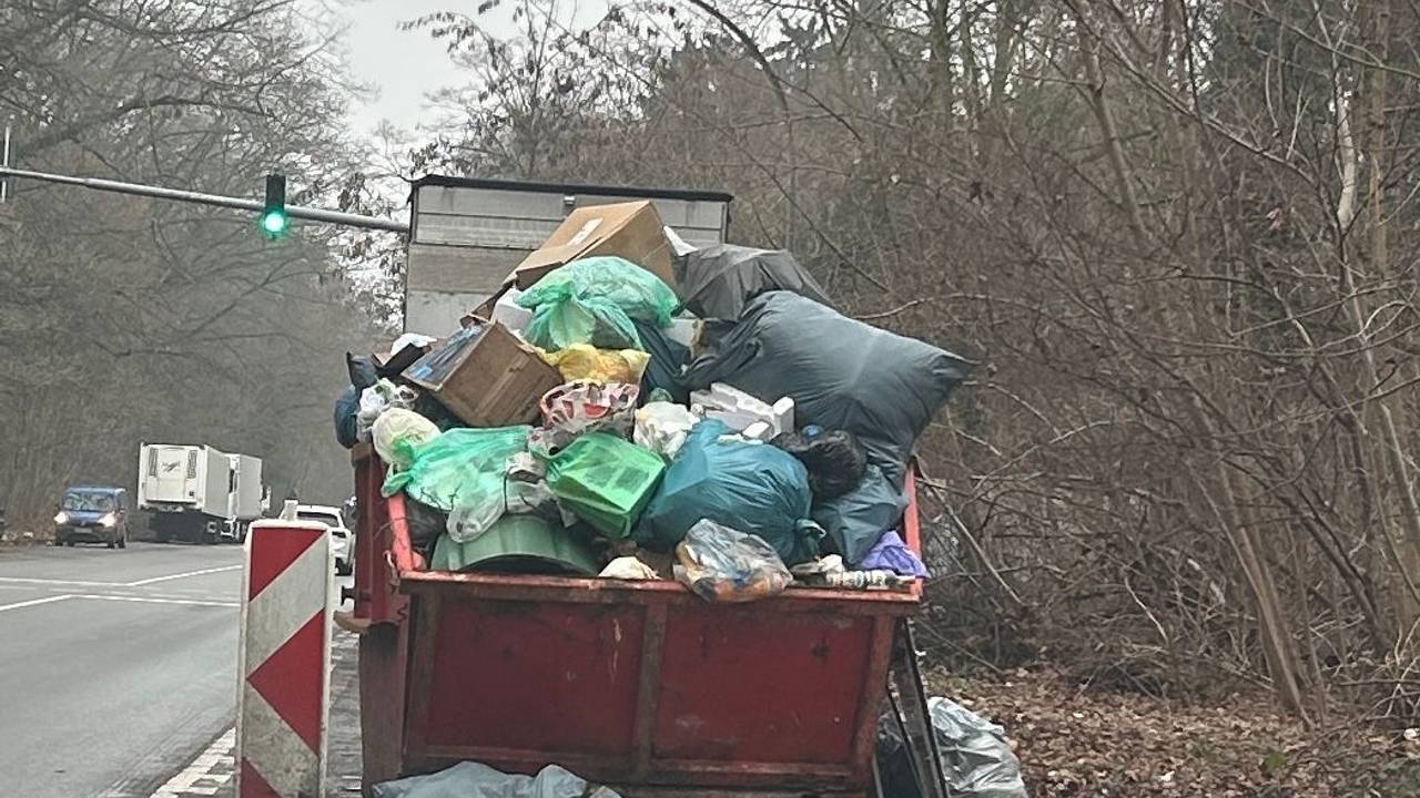 An einer Straße steht ein übervoller Müllcontainer, um ihn herum liegt ebenfalls Müll.