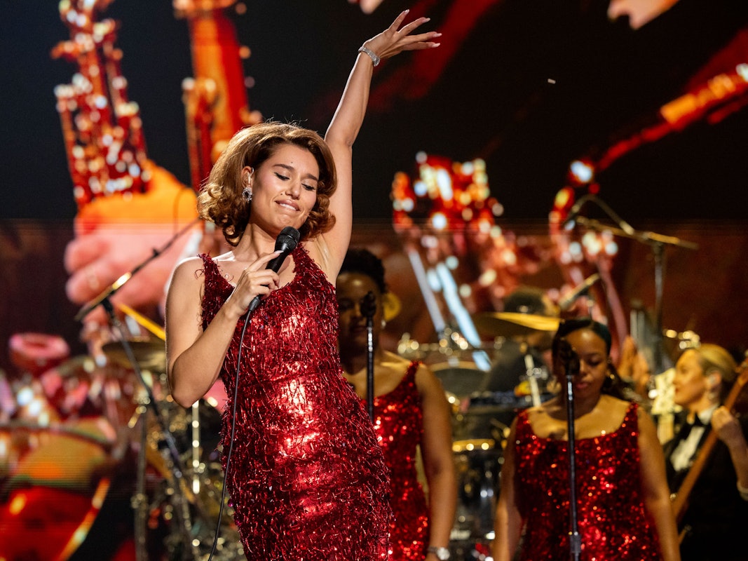 Sängerin Raye posiert in einem engen Pailettenkleid auf der Bühne.