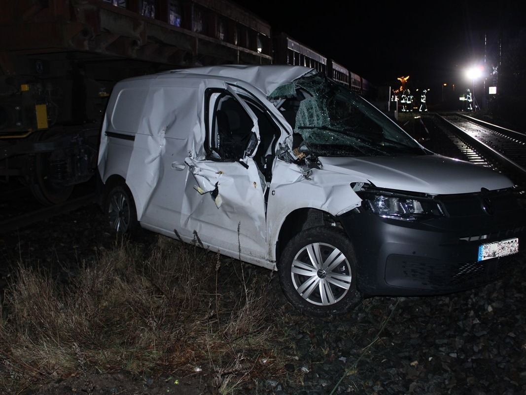 Ein demoliertes Auto steht neben einem Güterzug an einem Bahnübergang.