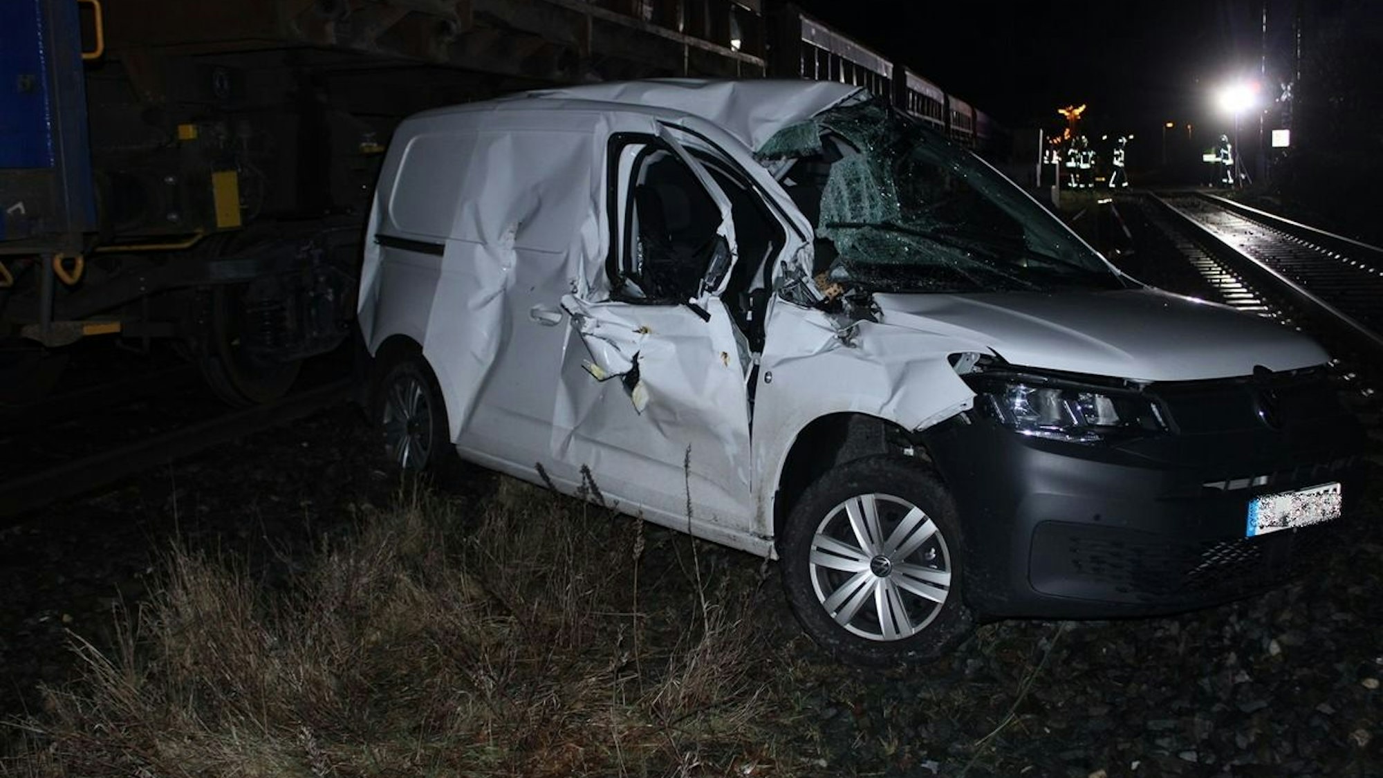 Ein demoliertes Auto steht neben einem Güterzug an einem Bahnübergang.