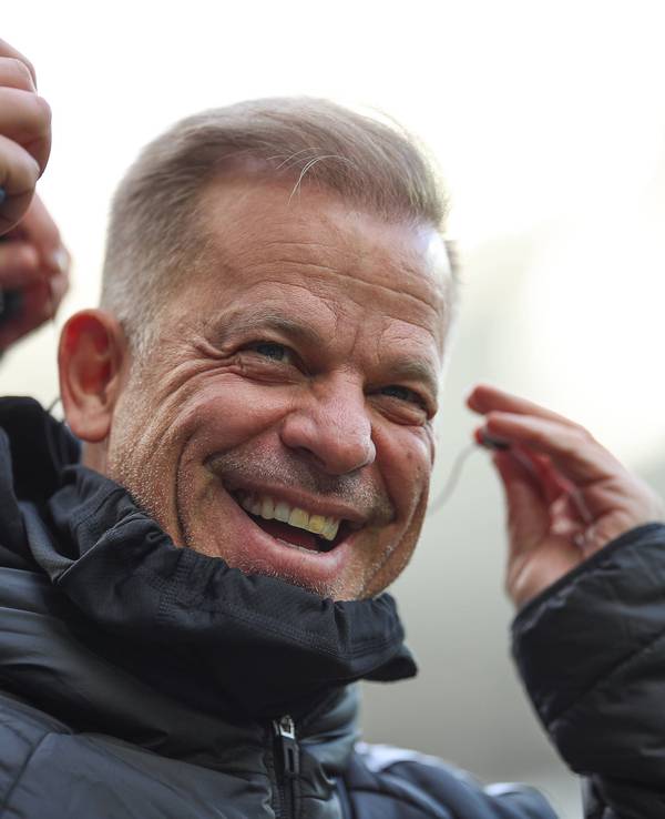 Markus Anfang lacht, während er sich mit der linken Hand einen Kopfhörer ins Ohr steckt.