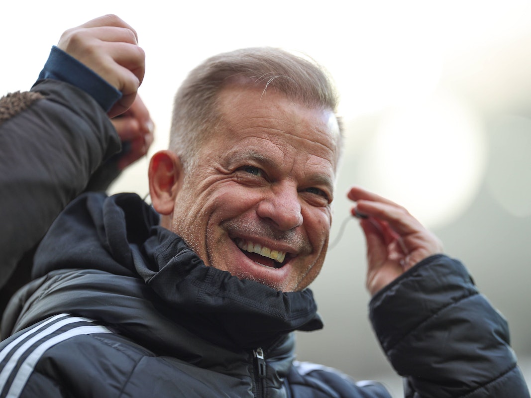 Markus Anfang lacht, während er sich mit der linken Hand einen Kopfhörer ins Ohr steckt.