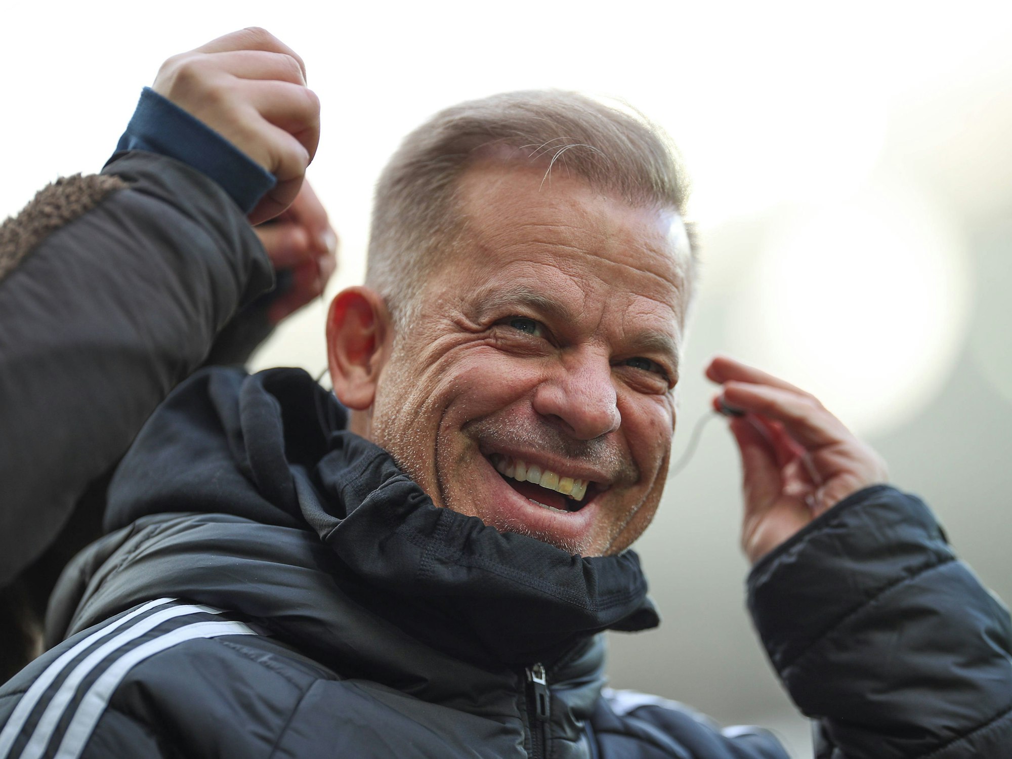 Markus Anfang lacht, während er sich mit der linken Hand einen Kopfhörer ins Ohr steckt.