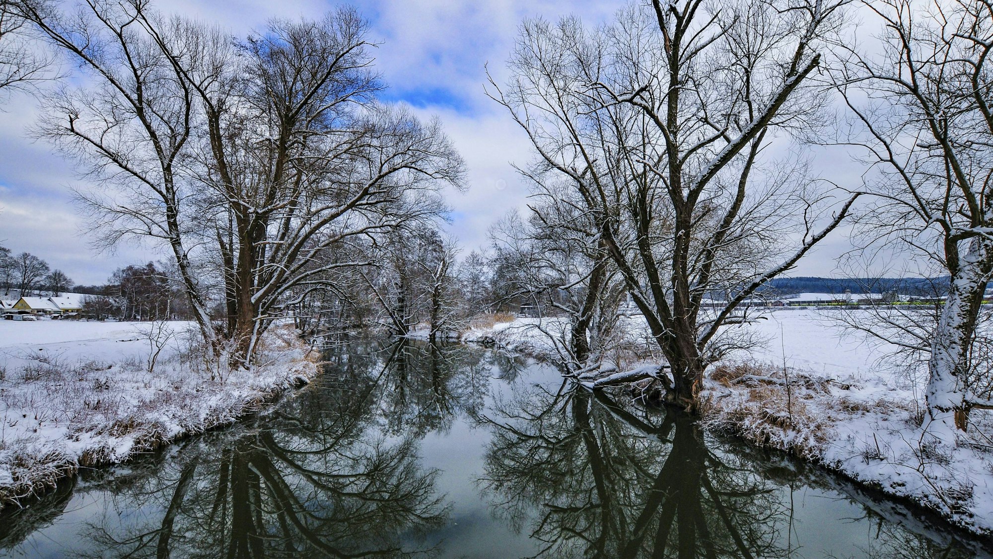 Verschneite Auenlandschaft mit Fluss und Bäumen