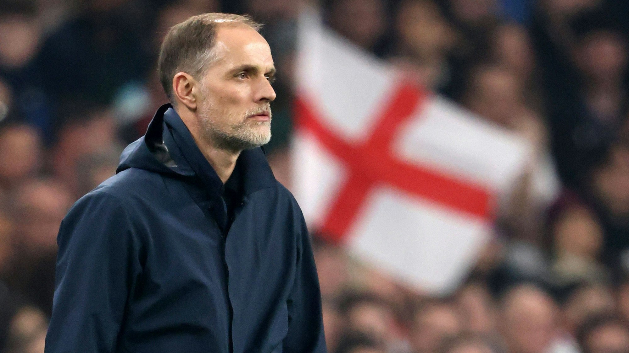 Thomas Tuchel schaut aufs Spielfeld, im Hintergrund ist eine England-Flagge zu sehen.