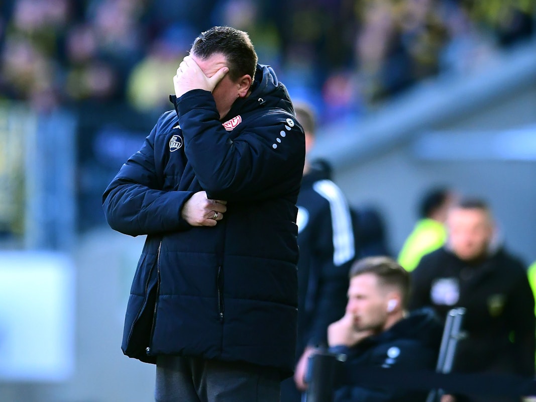 Uwe Koschinat hält sich bei einem Spiel von Rot-Weiss Essen die Hand vors Gesicht.