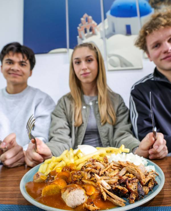 Nickolas Krugmann (von links), Antonija Dreznjak und Lukas Kampen sitzen vor ihren Taxi-Tellern in einem Imbiss in Essen. Pommes, Currywurst und dazu massenweise Gyros mit Zwiebeln: Im Ruhrgebiet sorgt der Taxi-Teller längst für Begeisterung bei Fast-Food-Fans.