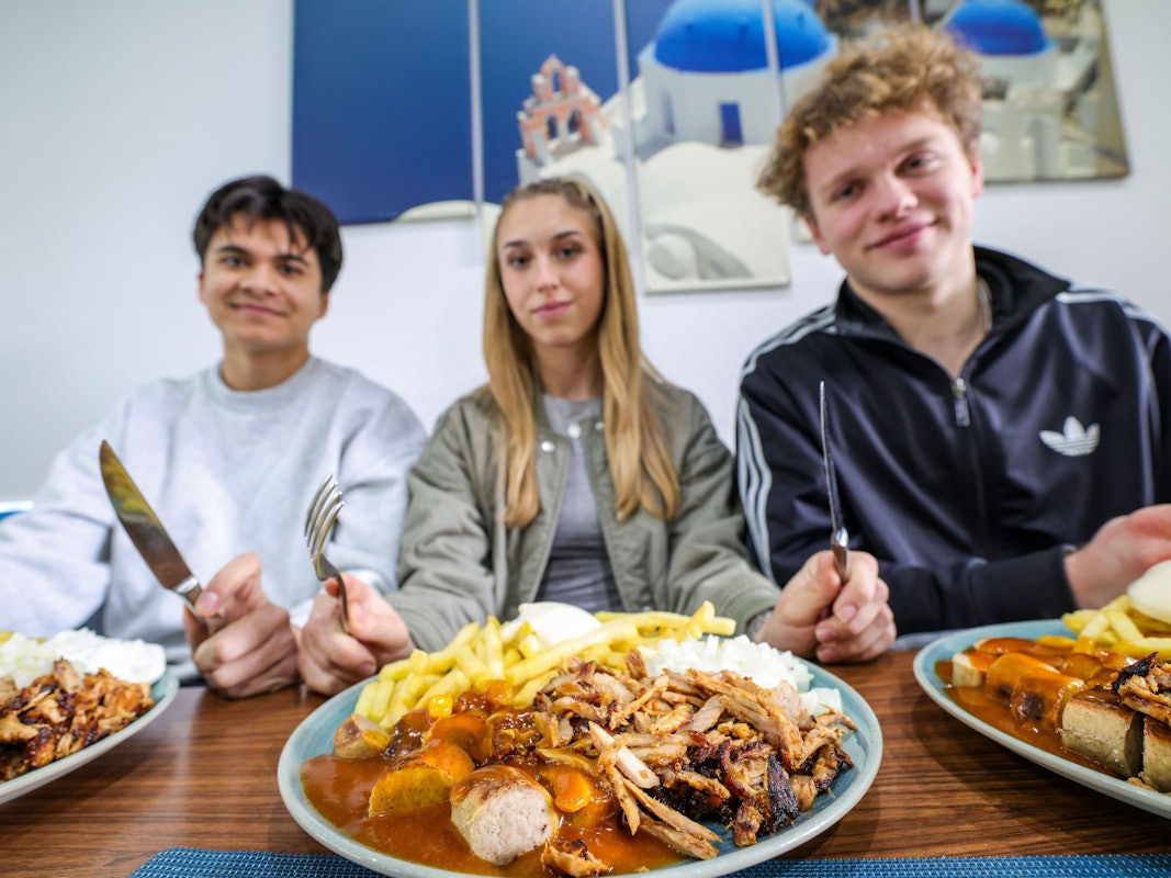 Nickolas Krugmann (von links), Antonija Dreznjak und Lukas Kampen sitzen vor ihren Taxi-Tellern in einem Imbiss in Essen. Pommes, Currywurst und dazu massenweise Gyros mit Zwiebeln: Im Ruhrgebiet sorgt der Taxi-Teller längst für Begeisterung bei Fast-Food-Fans.