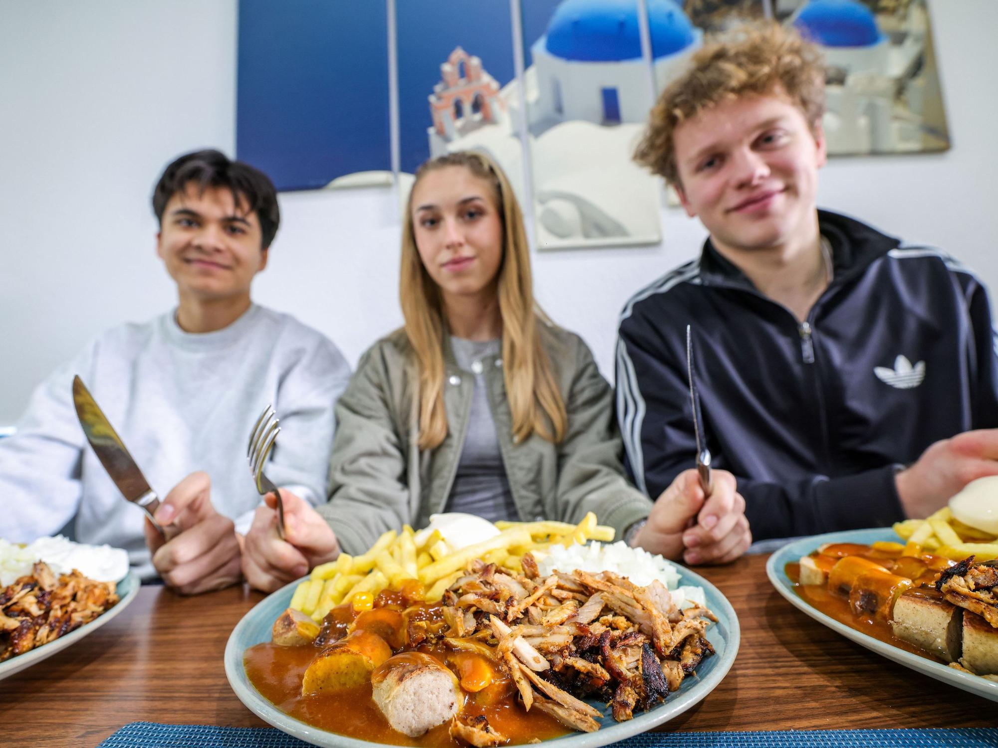 Nickolas Krugmann (von links), Antonija Dreznjak und Lukas Kampen sitzen vor ihren Taxi-Tellern in einem Imbiss in Essen. Pommes, Currywurst und dazu massenweise Gyros mit Zwiebeln: Im Ruhrgebiet sorgt der Taxi-Teller längst für Begeisterung bei Fast-Food-Fans.