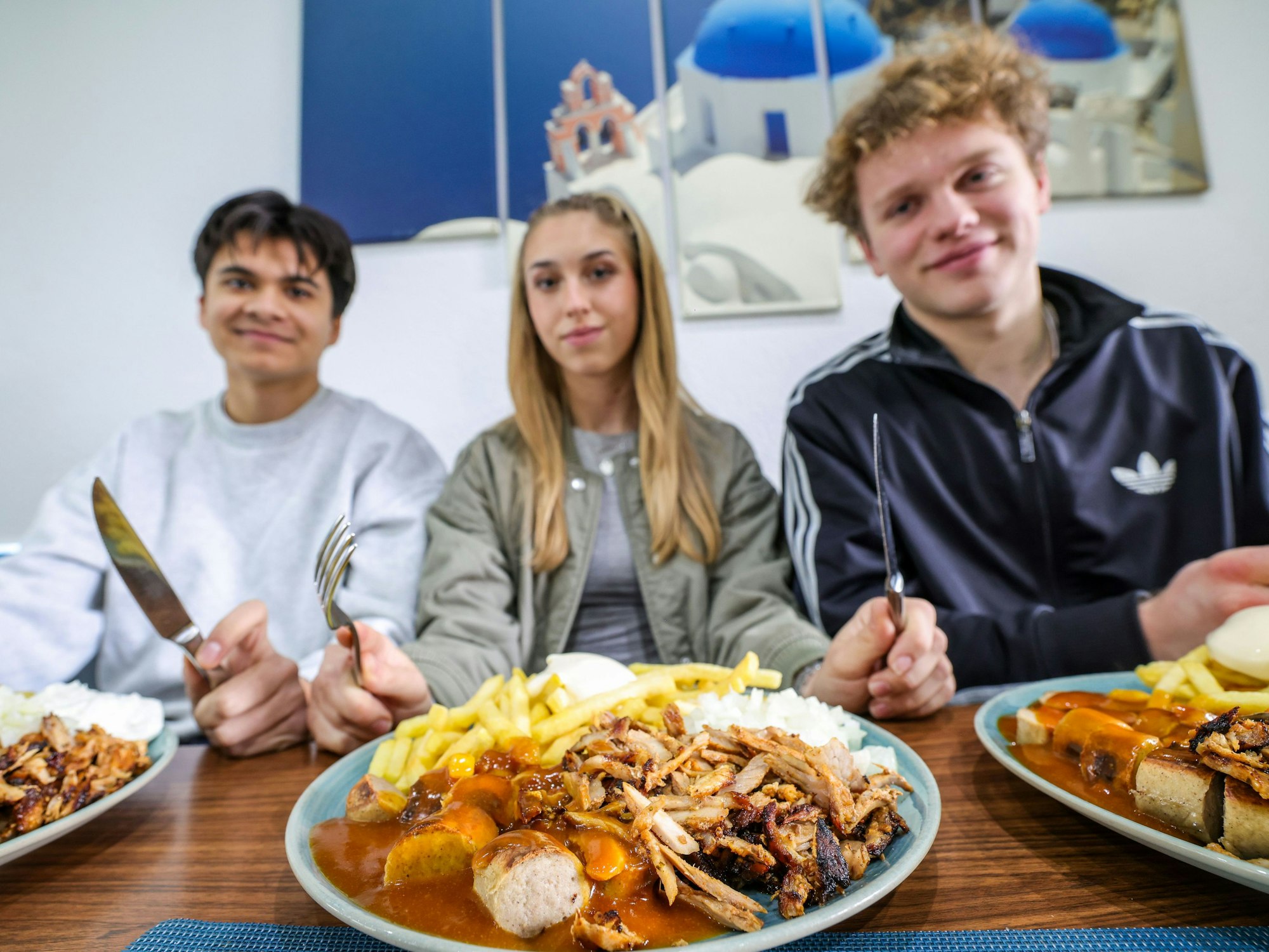 Nickolas Krugmann (von links), Antonija Dreznjak und Lukas Kampen sitzen vor ihren Taxi-Tellern in einem Imbiss in Essen. Pommes, Currywurst und dazu massenweise Gyros mit Zwiebeln: Im Ruhrgebiet sorgt der Taxi-Teller längst für Begeisterung bei Fast-Food-Fans.