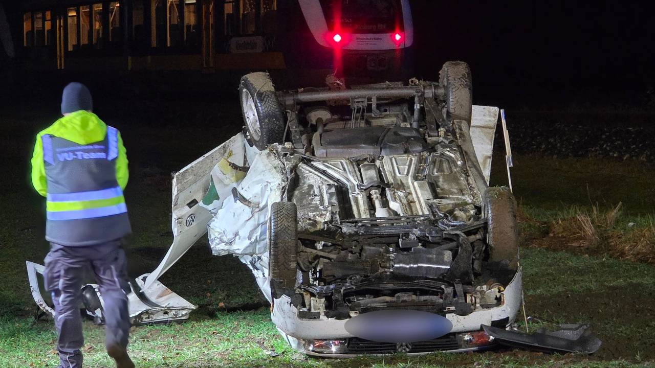 Ein Polizist steht nach einem Unfall neben einem auf dem Dach liegenden Auto. Beim Überqueren eines unbeschrankten Bahnübergangs war der Wagen von einem Zug erfasst worden. Der 18-jährige Fahrer erlag im Krankenhaus seinen Verletzungen.