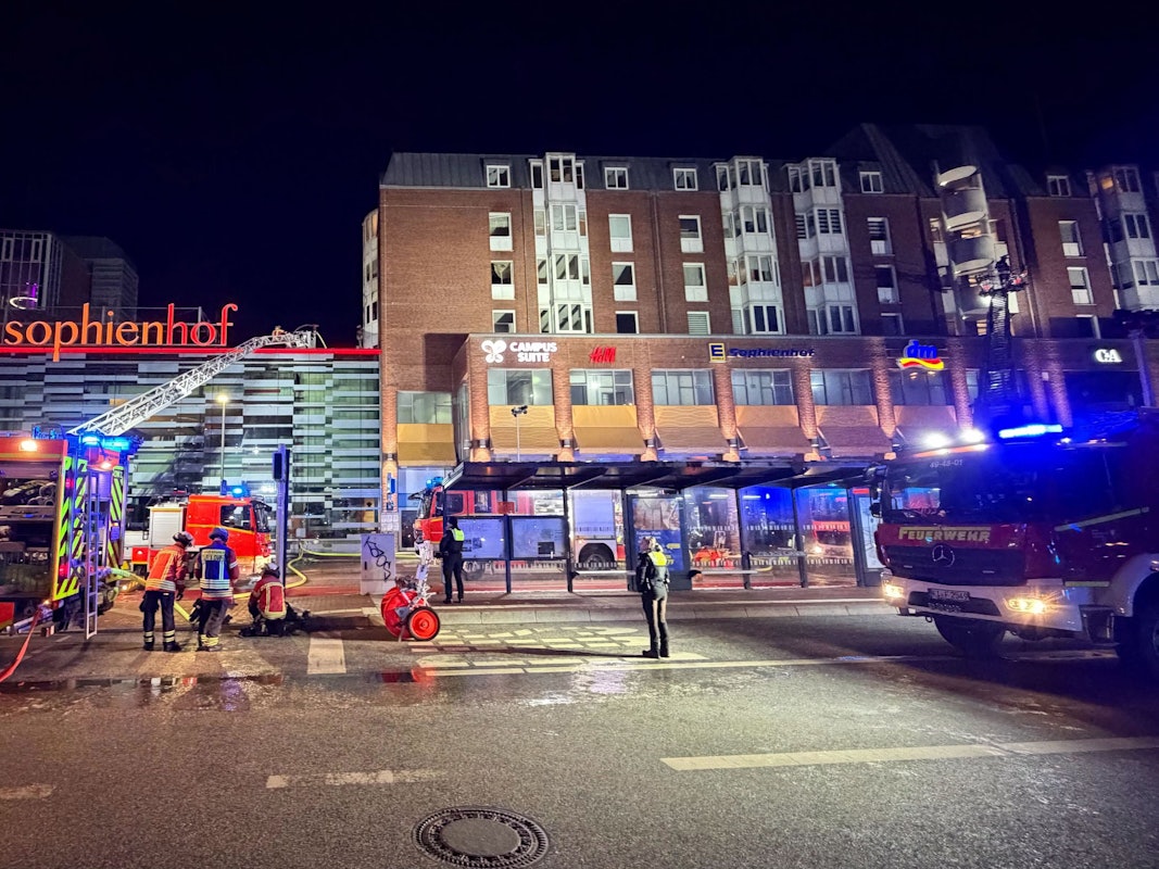 Einsatzkräfte der Feuerwehr arbeiten auf einer Drehleiter an einem Wohnhaus neben dem Einkaufszentrum Sophienhof in der Kieler Innenstadt.