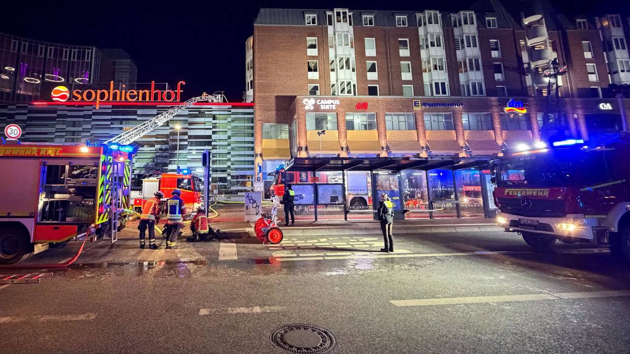 Einsatzkräfte der Feuerwehr arbeiten auf einer Drehleiter an einem Wohnhaus neben dem Einkaufszentrum Sophienhof in der Kieler Innenstadt.