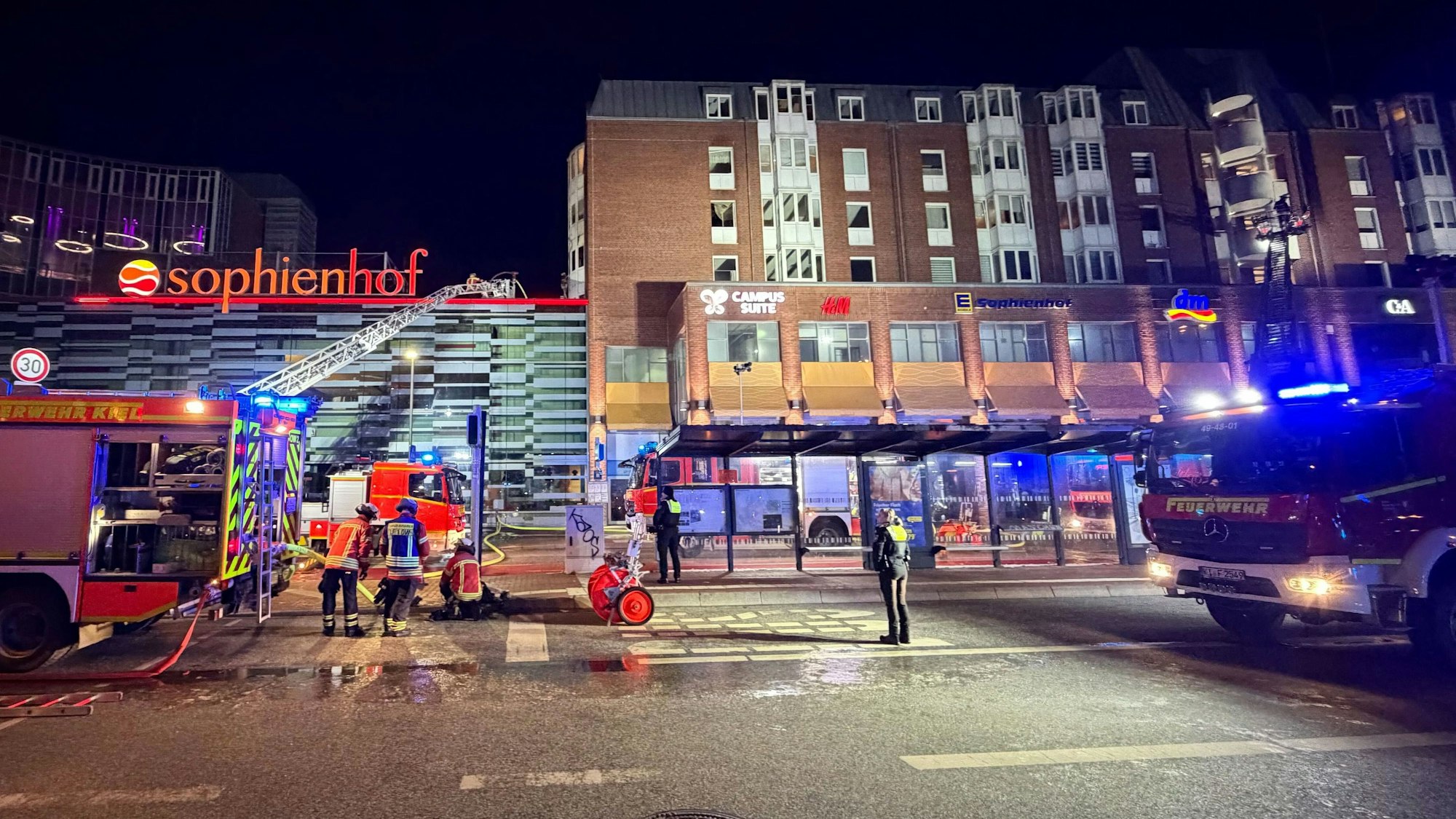 Einsatzkräfte der Feuerwehr arbeiten auf einer Drehleiter an einem Wohnhaus neben dem Einkaufszentrum Sophienhof in der Kieler Innenstadt.