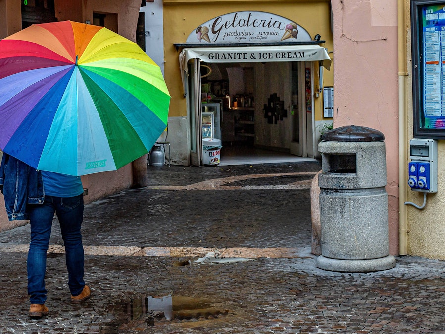 Person und bunter Regenschirm auf nasser Straße.