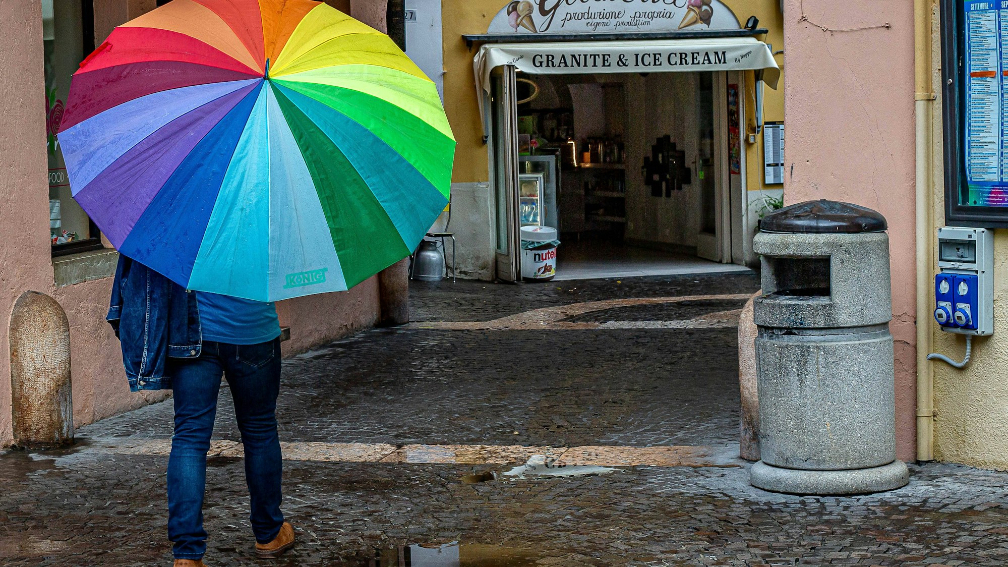 Person und bunter Regenschirm auf nasser Straße.