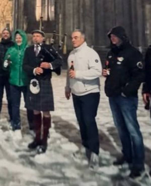 Ein Dudelsackspieler steht vor dem Dom, mehrere Menschen stehen neben ihm.