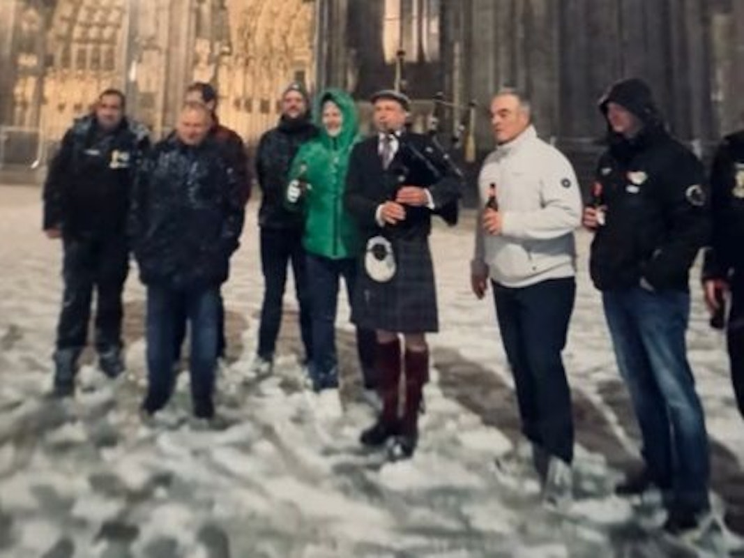 Ein Dudelsackspieler steht vor dem Dom, mehrere Menschen stehen neben ihm.