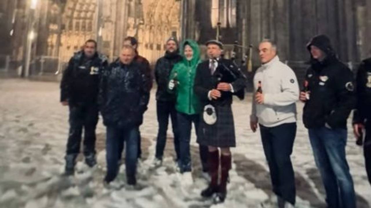 Ein Dudelsackspieler steht vor dem Dom, mehrere Menschen stehen neben ihm.
