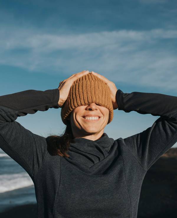 Glückliche Frau zieht sich an einem Strand bei Sonnenschein die Mütze über beide Augen