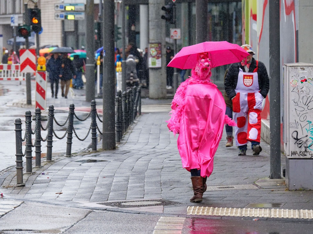 Eine Karnevalistin ist bei Regen mit einem knallpinken Regenschirm und -poncho unterwegs.