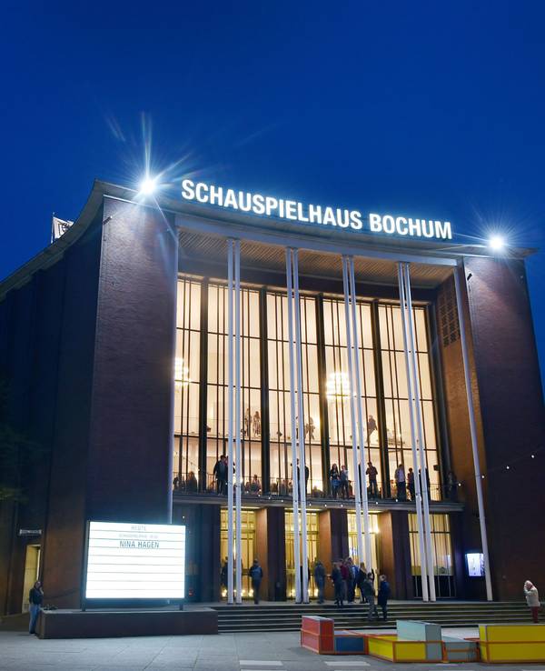 Besucherinnen und Besucher stehen während einer Pause vor dem Haupteingang des Schauspielhauses Bochum an der Königsallee.