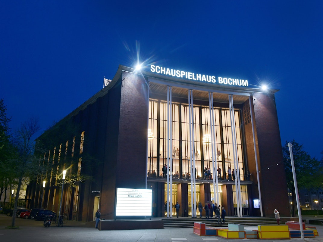Besucherinnen und Besucher stehen während einer Pause vor dem Haupteingang des Schauspielhauses Bochum an der Königsallee.