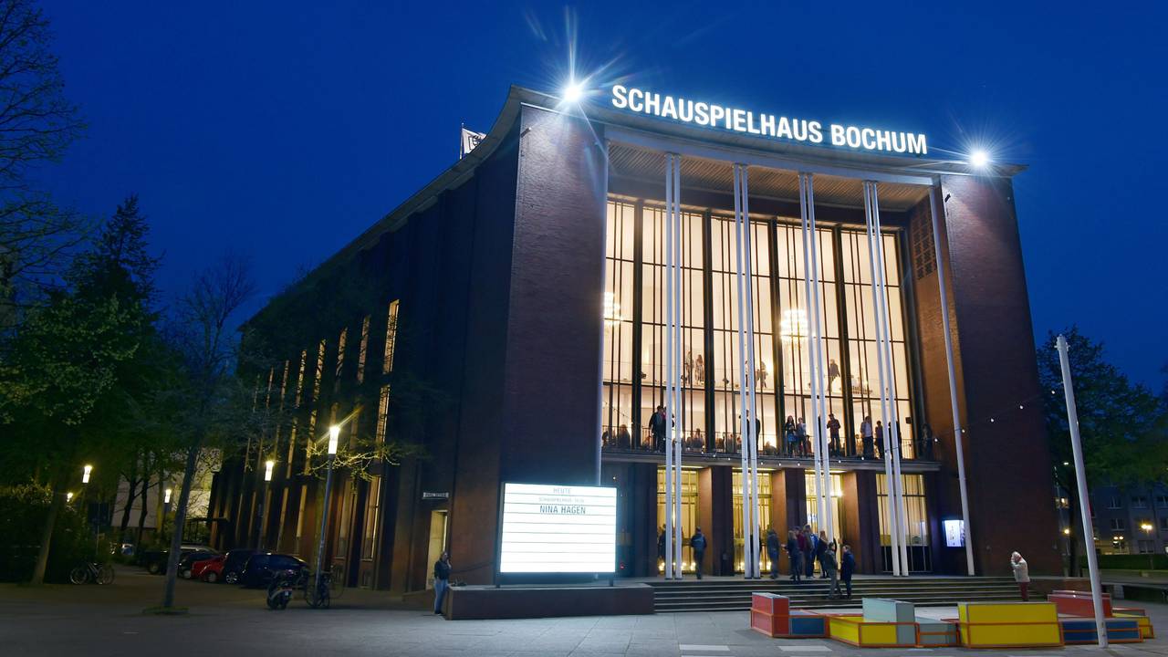 Besucherinnen und Besucher stehen während einer Pause vor dem Haupteingang des Schauspielhauses Bochum an der Königsallee.