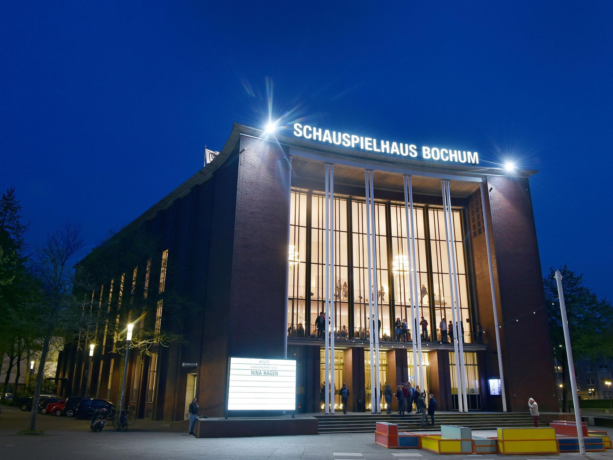 Besucherinnen und Besucher stehen während einer Pause vor dem Haupteingang des Schauspielhauses Bochum an der Königsallee.
