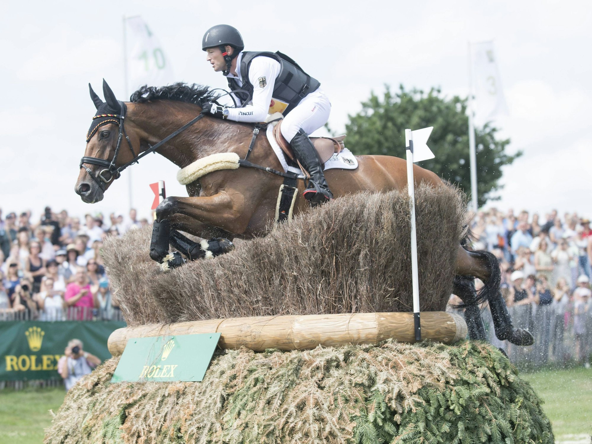 Michael Jung springt mit seinem Pferd Sam über ein Hindernis im Gelände.