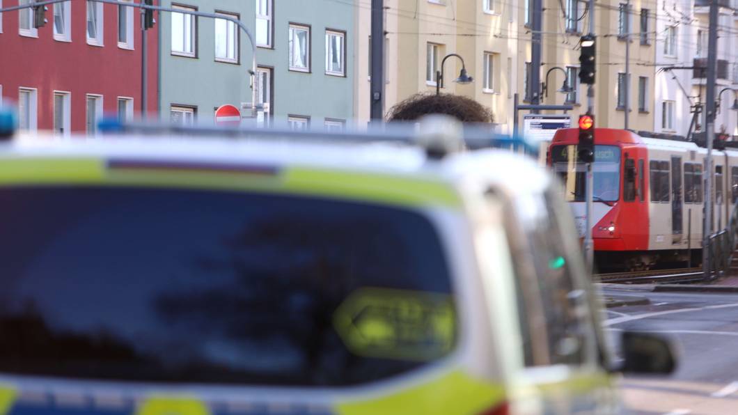 Ein Polizeifahrzeug steht auf einer Straße, im Hintergrund eine Stadtbahn.