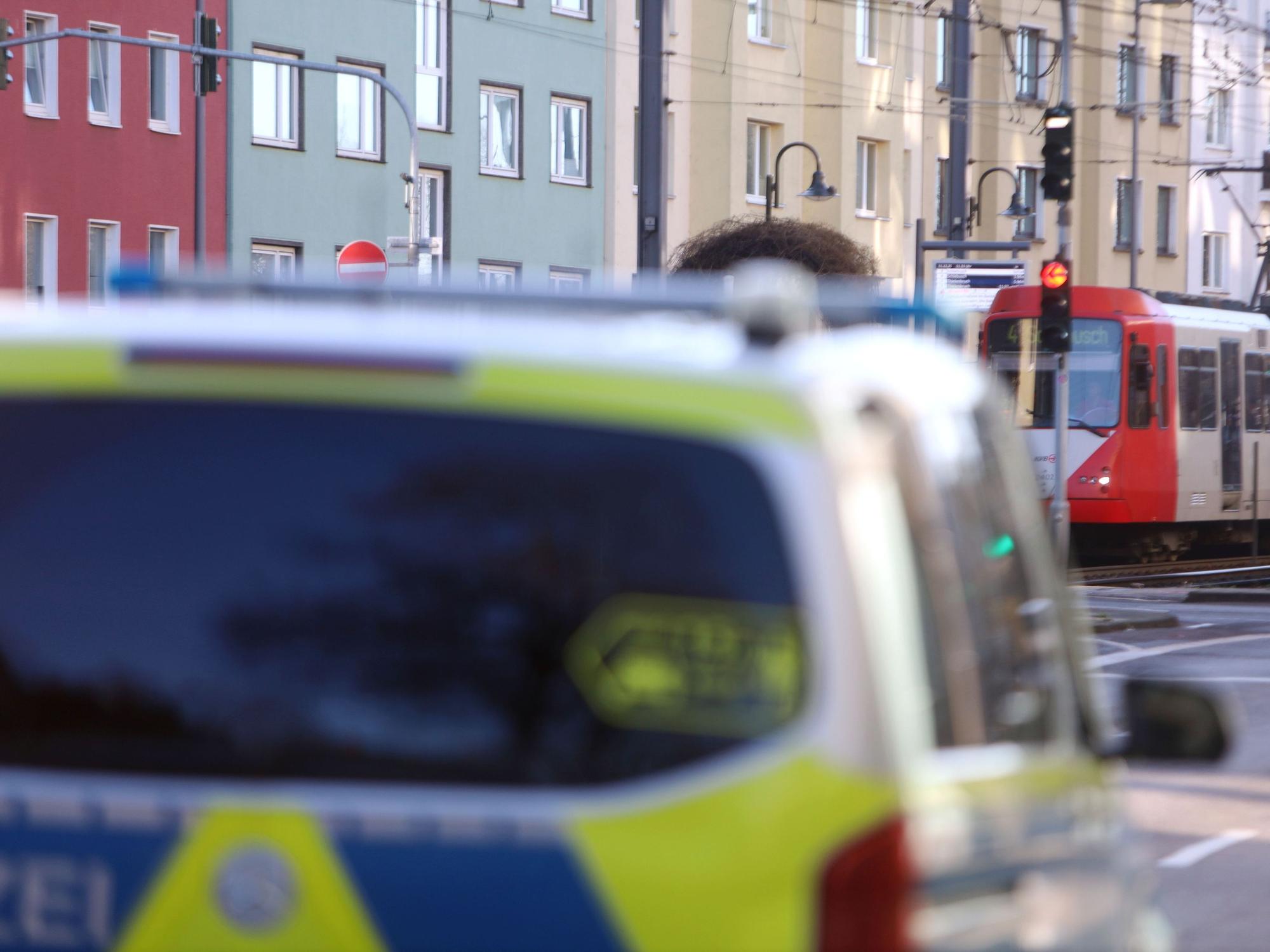 Ein Polizeifahrzeug steht auf einer Straße, im Hintergrund eine Stadtbahn.