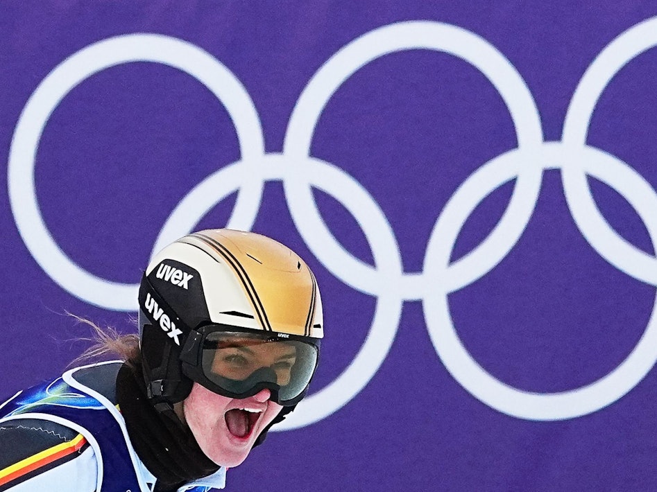 Emma Aicher jubelt im Ziel. Im Hintergrund sind die Olympischen Ringe zu sehen.