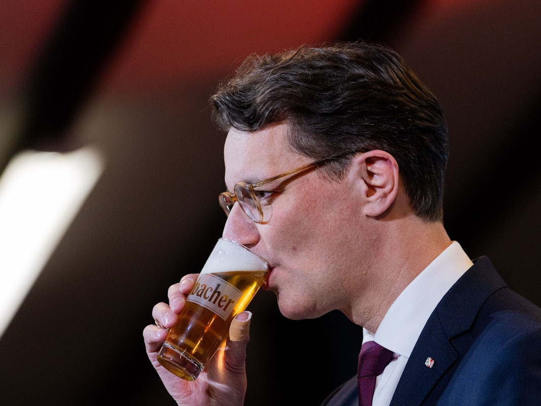 Hendrik Wüst (CDU) trinkt ein Bier bei seiner Rede beim Politischen Aschermittwoch in der Schützenhalle Kirchveischede.