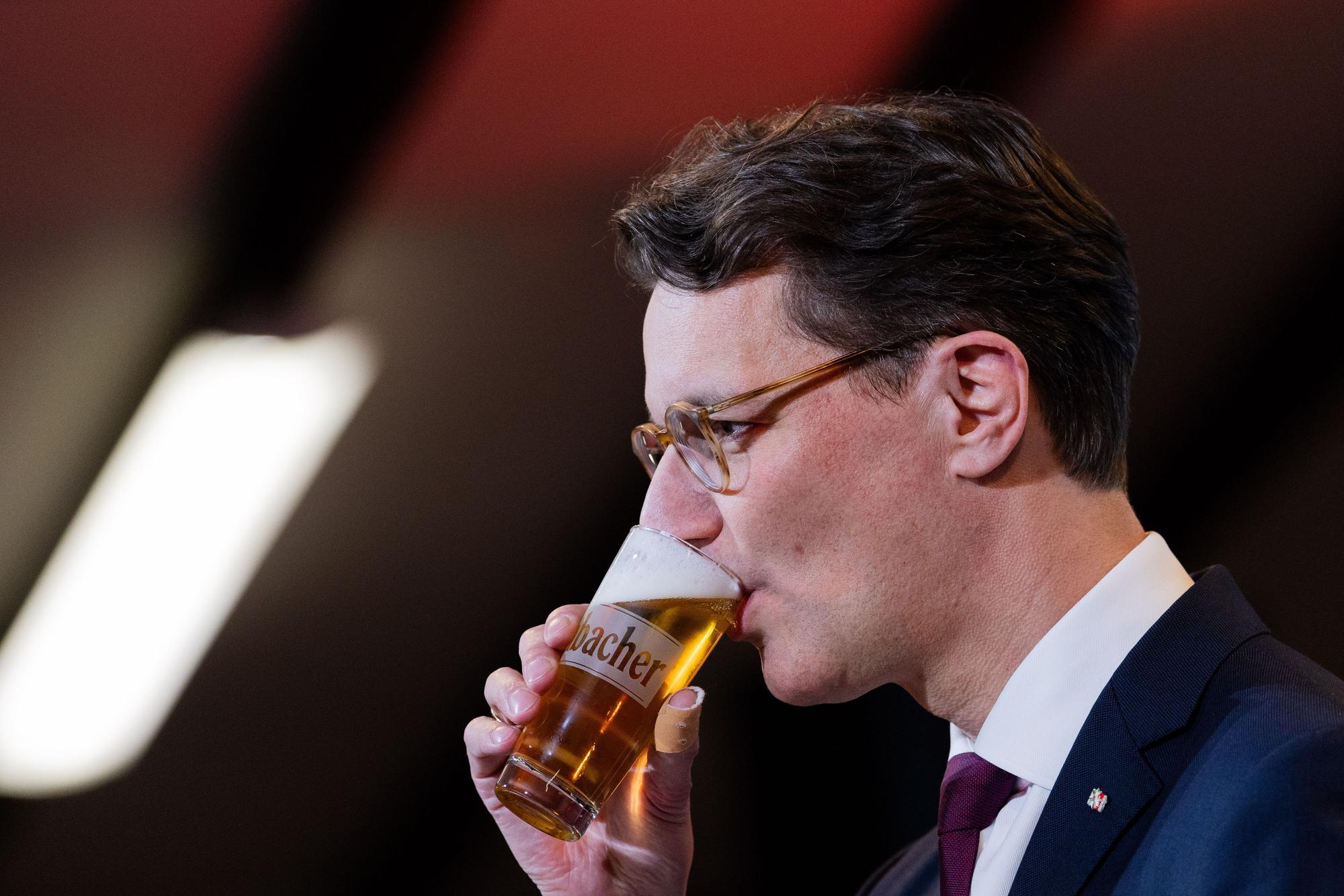 Hendrik Wüst (CDU) trinkt ein Bier bei seiner Rede beim Politischen Aschermittwoch in der Schützenhalle Kirchveischede.