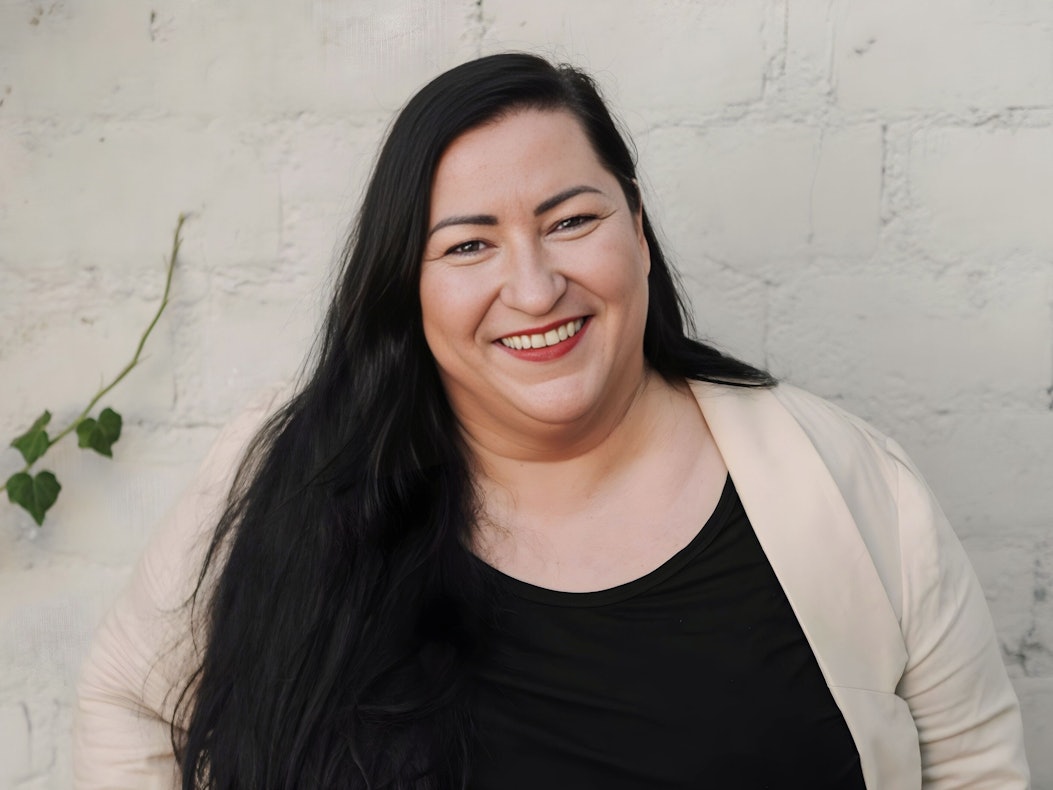 Foto von Vanessa Spaleck lächelnd vor einer weißen Mauer.