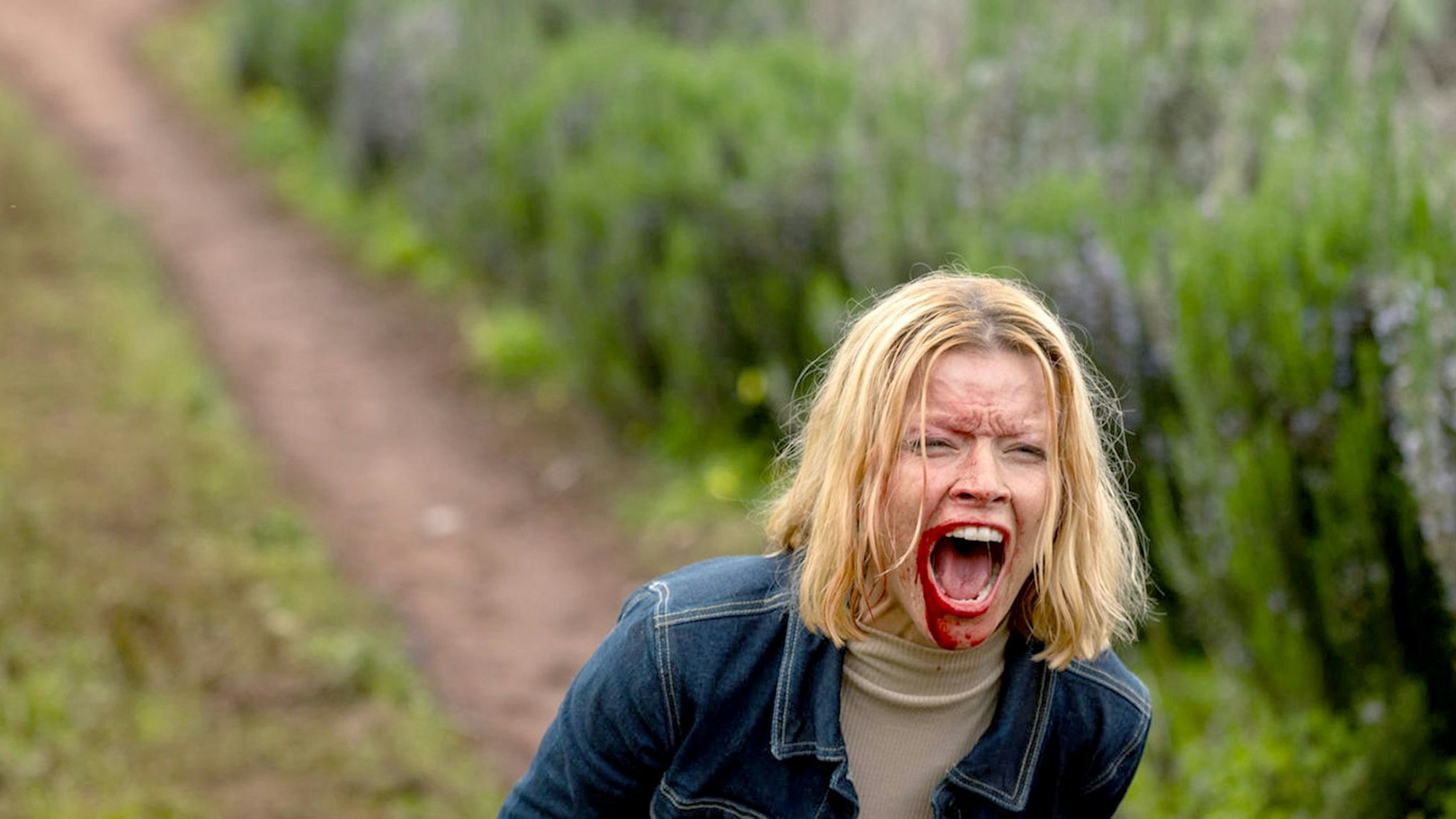 Eine blonde Frau reißt ihren blutverschmierten Mund weit auf.